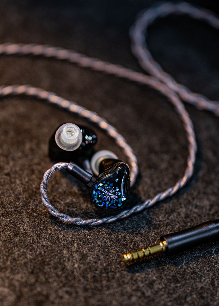 Artistic shot of in-ear monitors with a braided cable on a dark textured surface, highlighting modern audio design.