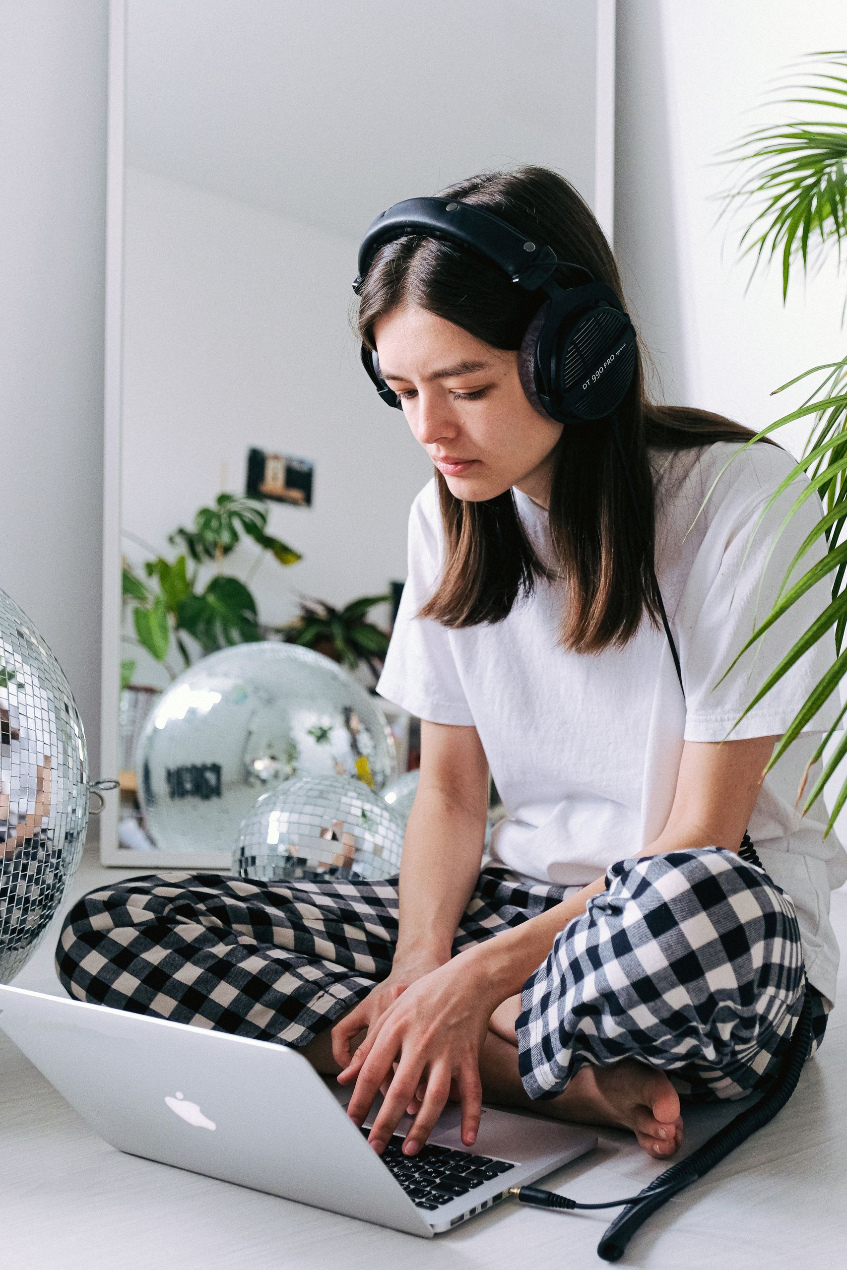 Young woman using a laptop and headphones at home, surrounded by disco balls, in a cozy workspace.
